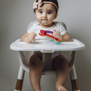 Cute baby girl with colorful toy sitting in high chair. Perfect for childcare themes.