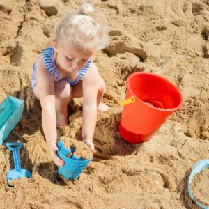 Adorable child playing in the sand with colorful toys on a sunny beach day.