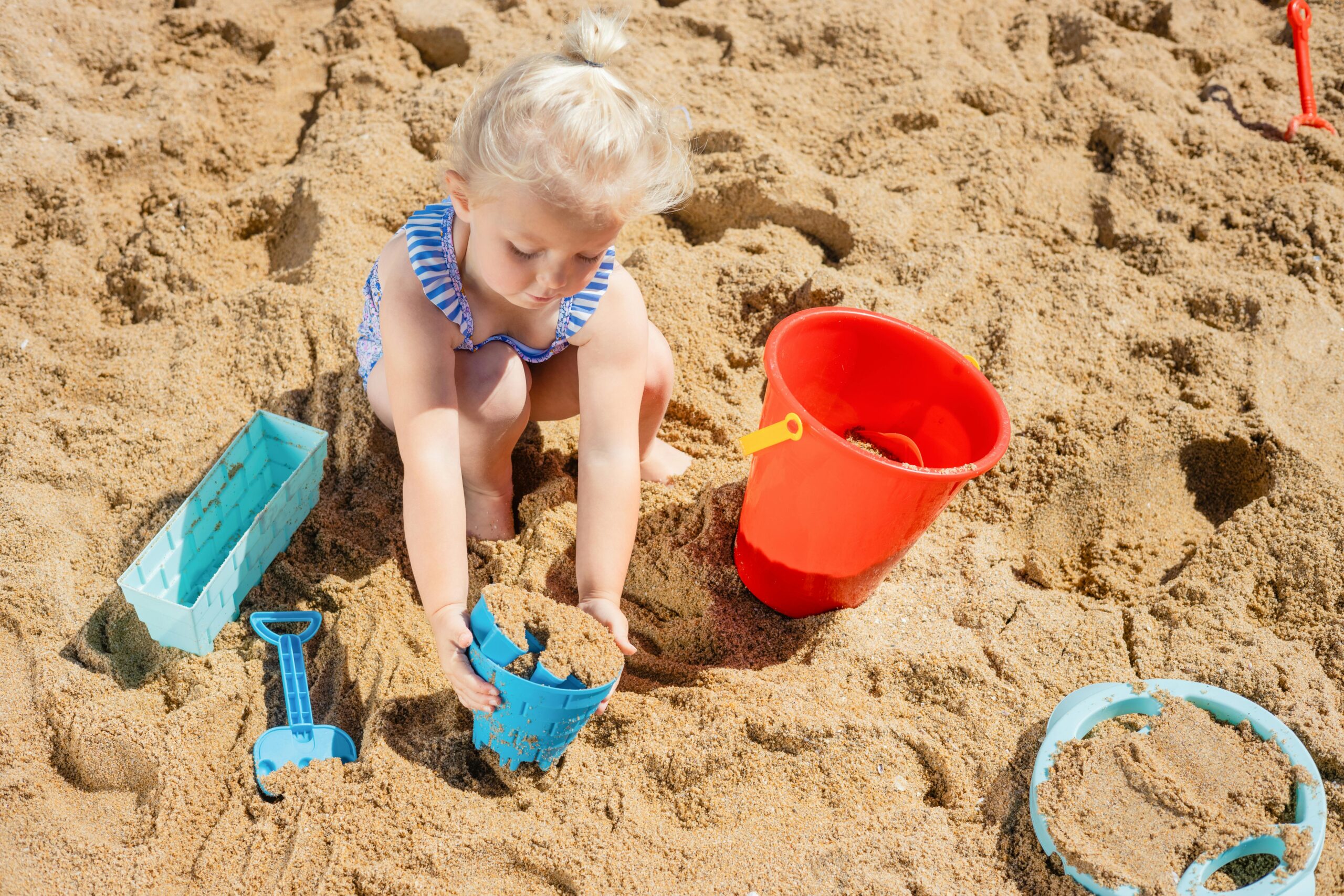 Adorable child playing in the sand with colorful toys on a sunny beach day.